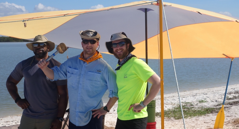 three people smile at the camera while standing under a shelter on a beach